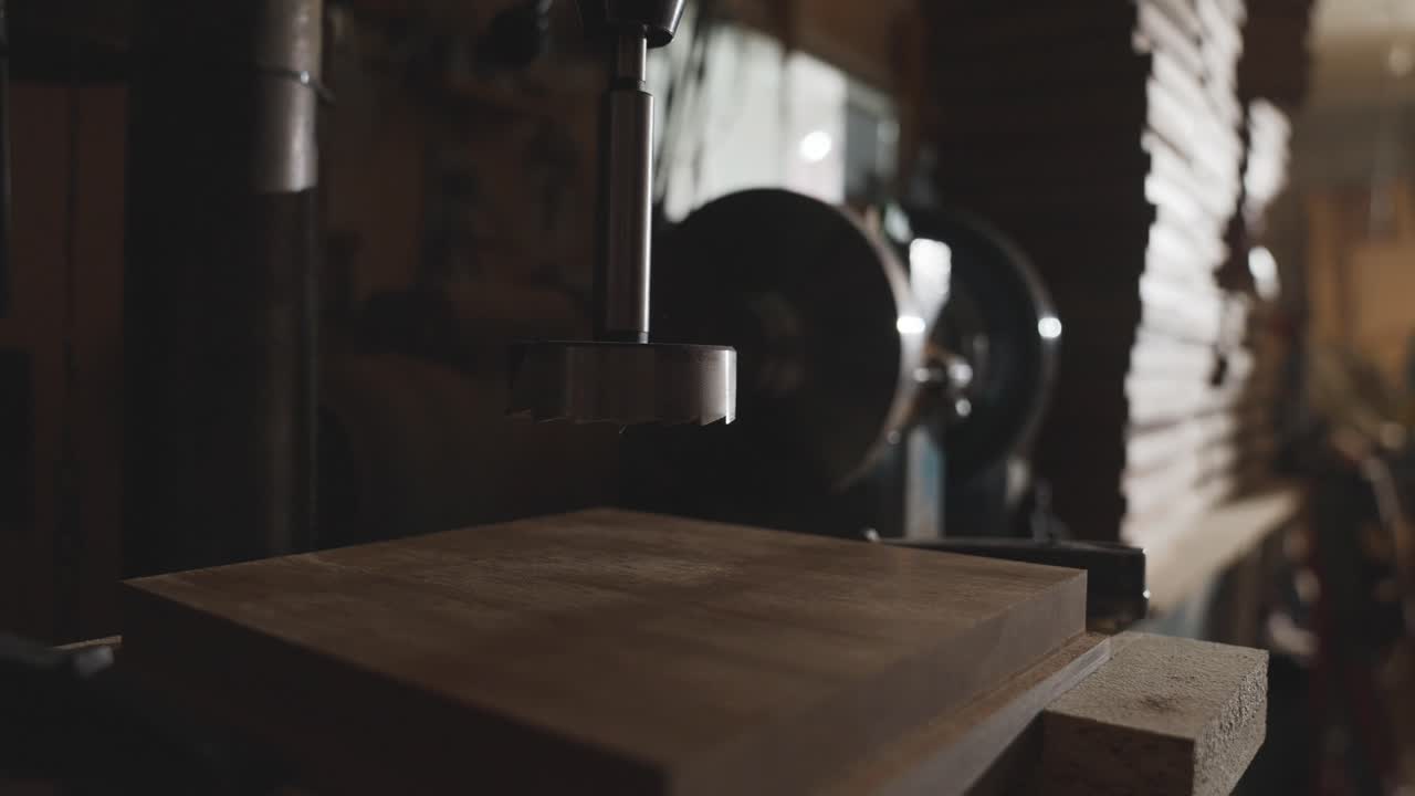 Craftsman placing wooden board under industrial milling machine with drill bit