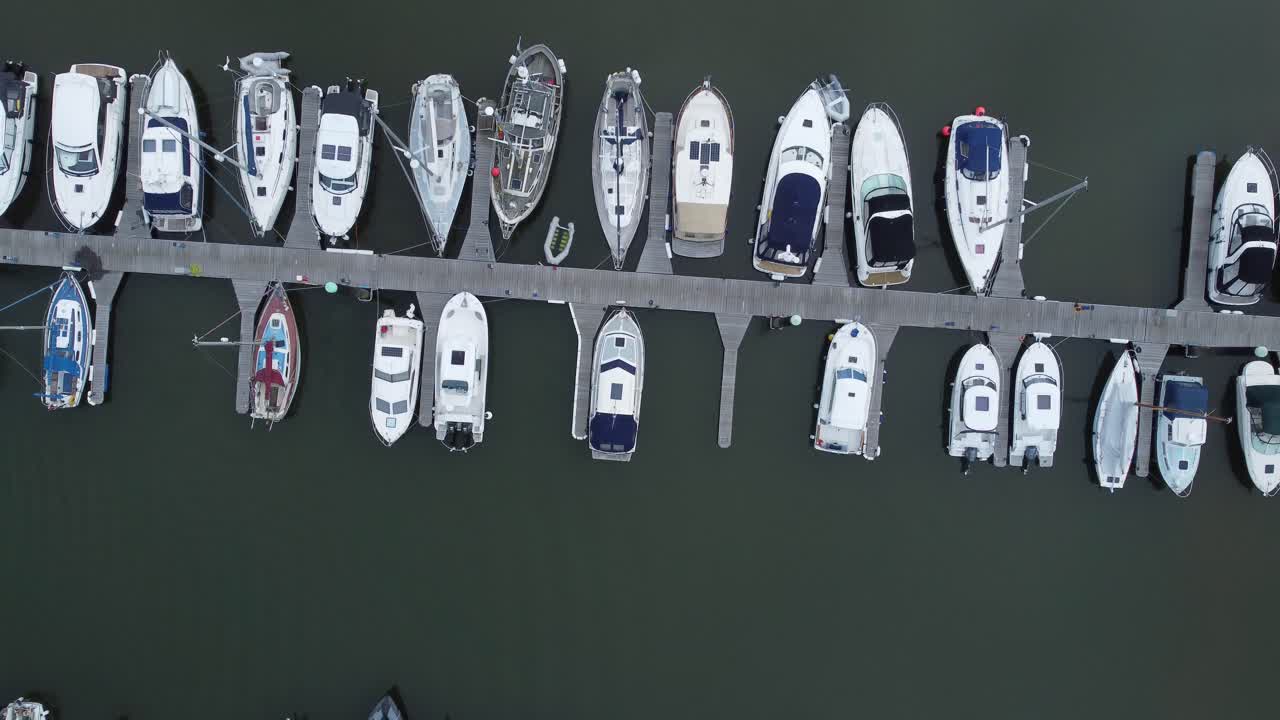 Top down aerial drone view above luxury moored private marina sailing ships and yacht boats moving forwards