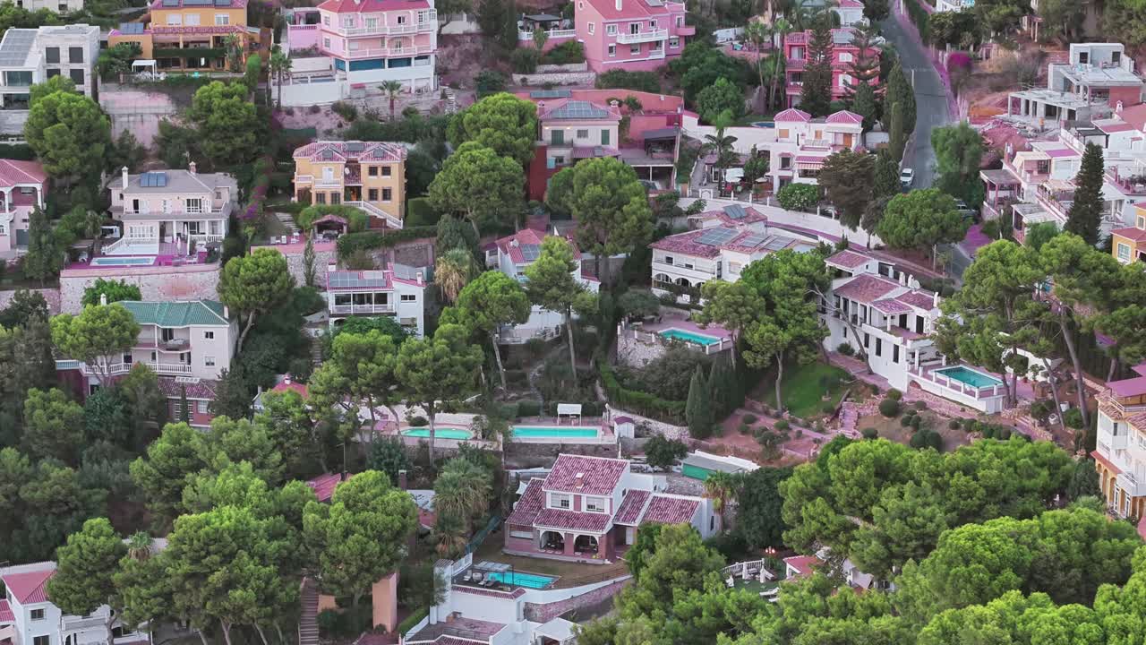 Aerial view of hillside residential area in Málaga, Spain. Colorful houses surrounded by lush green trees create a Mediterranean urban landscape blending nature and architecture