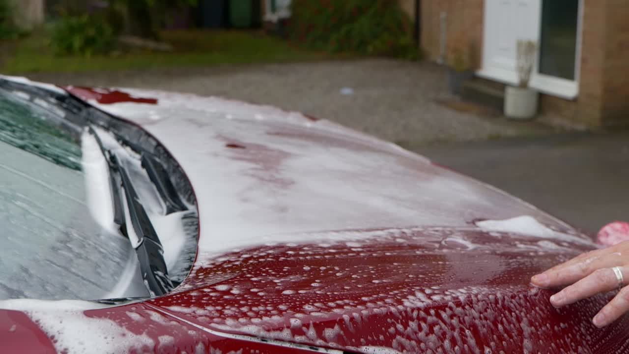 Lavaggio di un'auto elettrica rosso ciliegia scuro con schiuma da neve e shampoo con un guanto da lavaggio in microfibra rosso - vicino alla fotocamera