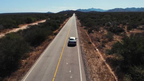 aerial of car driving on a straight road through desert landscape