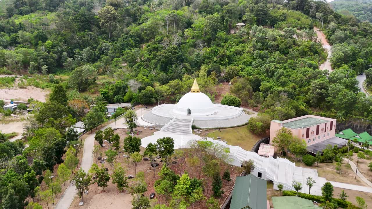 las imágenes de drones capturan un sereno templo budista rodeado de exuberante vegetación en phuket, tailandia, destacando su belleza arquitectónica y su entorno tranquilo.