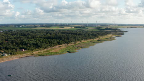 Aerial-panoramic-footage-of-coastal-landscape,-woods-and-grasslands-in-countryside.-Wind-park-providing-green-sustainable-energy.-Denmark