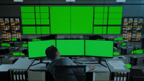 vista trasera de un hombre asiático aburrido trabajando con múltiples monitores de computadora en la oficina