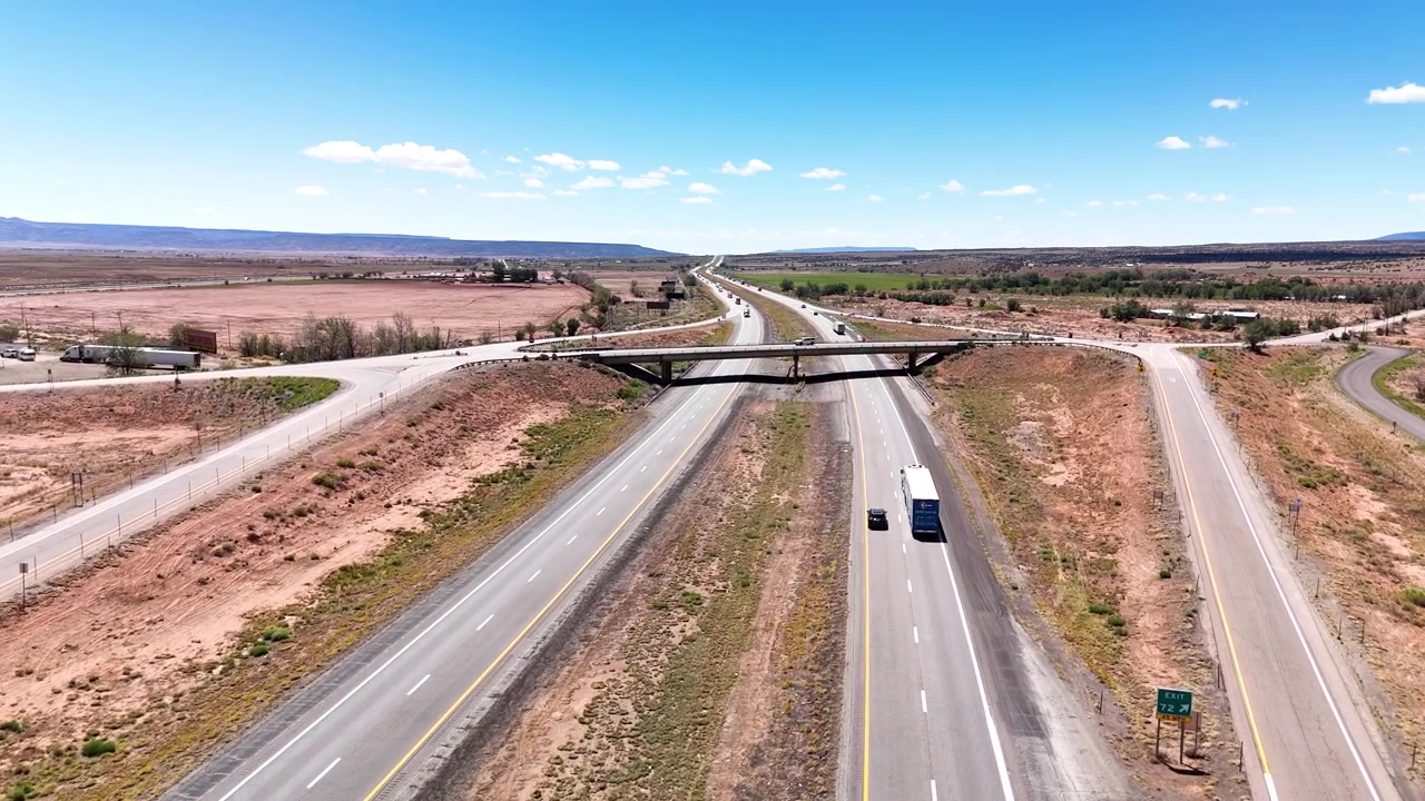 Cars driving on a US interstate highway across a sun-drenched desert, viewed from a high-angle drone perspective