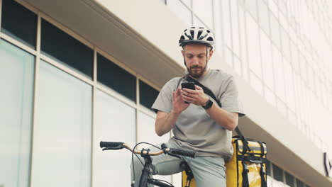 food delivery guy wearing thermal backpack taking a look at his smartphone on his bike