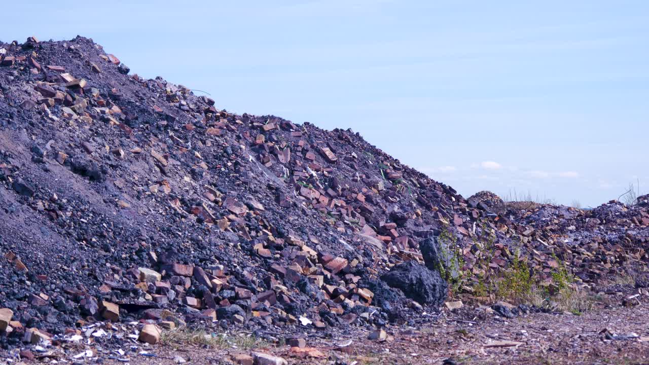 Utvendig utsikt over forlatt sovjetisk smelteverk for tungmetallurgi, området Liepajas Metalurgs, hauger av rusk og rask, gamle murstein, solfylt dag, halvtotal.