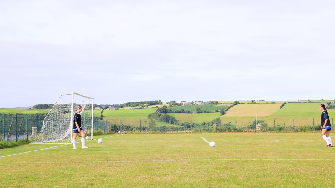 Female soccer players, walking, practicing kicking and passing ball on pitch, copy space