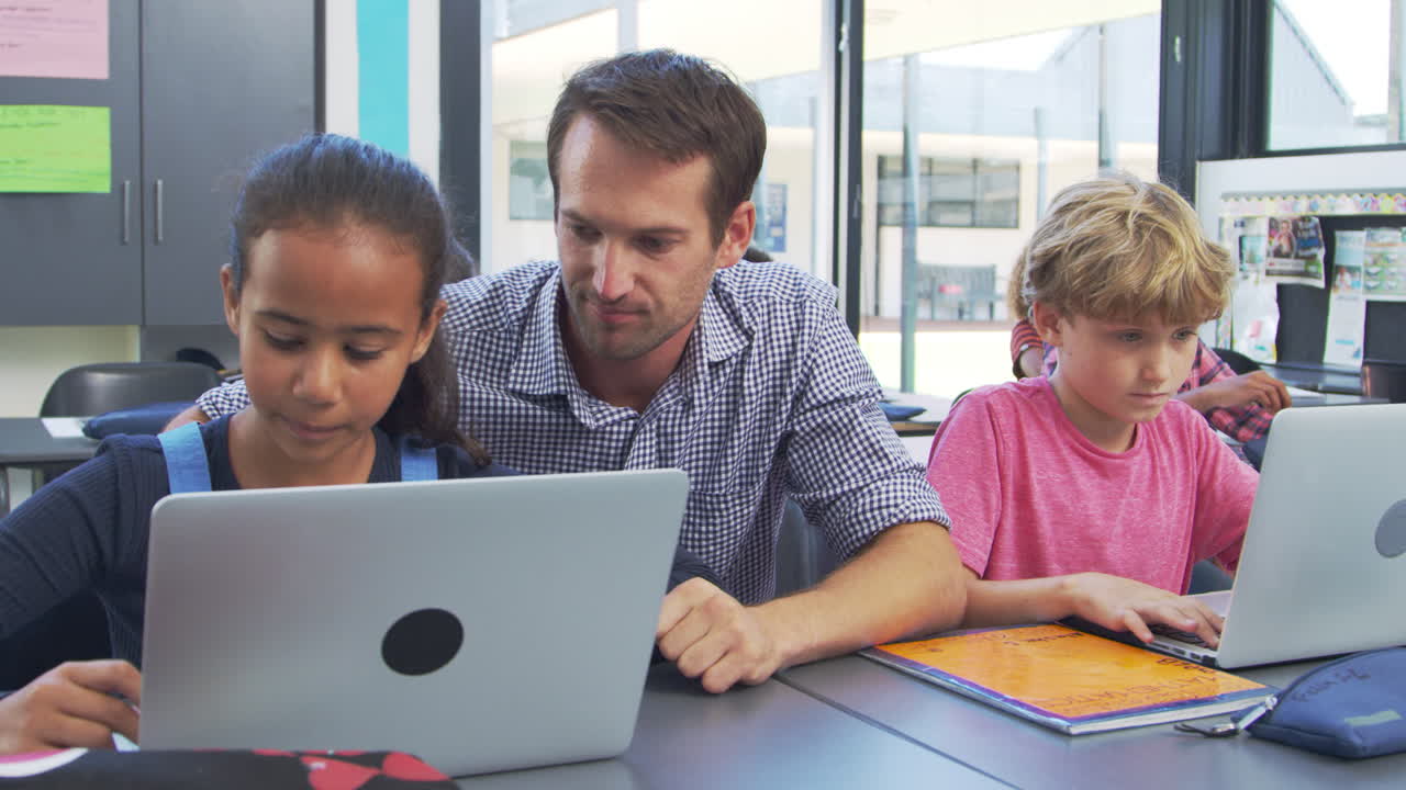 maestro ayudando a los estudiantes jóvenes a usar computadoras portátiles en clase