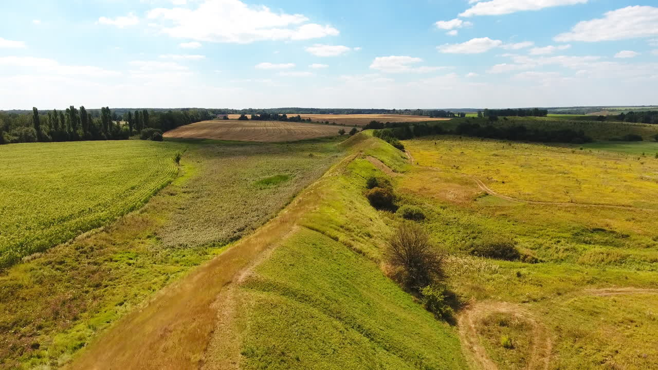Summer green landscape under blue skies. Long hill separating meadows from agricultural farmlands. Top view.