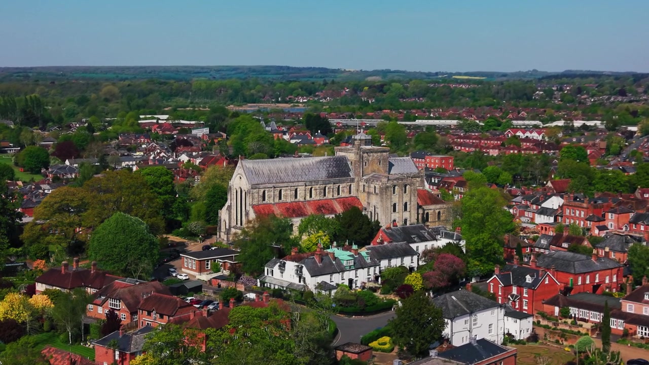 Drohnen-Luftaufnahme der Romsey Abbey, umgeben von Dächern, Bäumen und dem historischen Stadtzentrum von Romsey in Hampshire, England