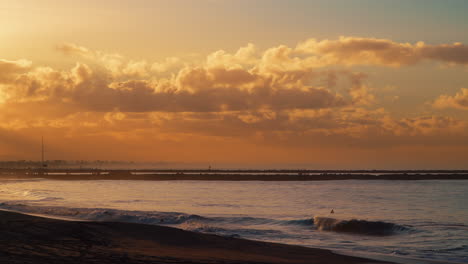 Amanecer-Dorado-Sobre-La-Playa-De-Focas-Con-Olas-Serenas-Y-Un-Horizonte-Despejado,-Reflejando-Colores-Cálidos-En-El-Agua,-Toma-Amplia