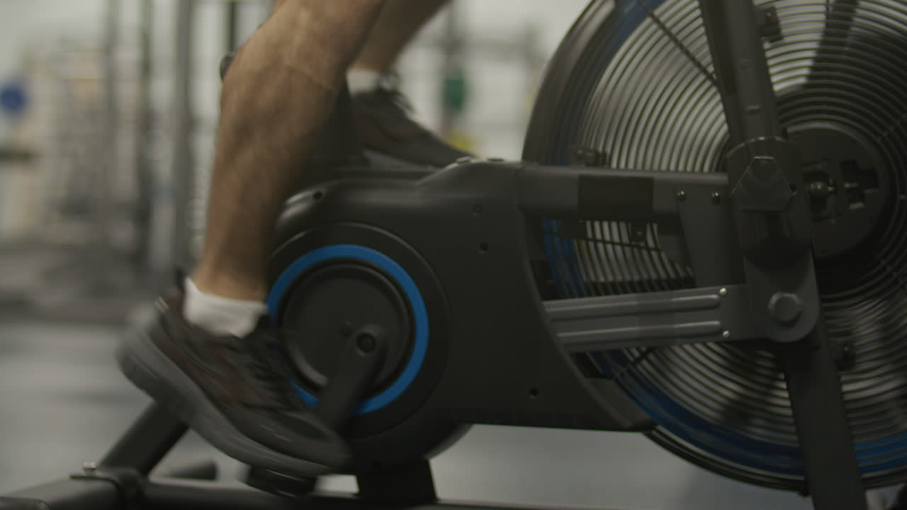 Close-Up of Male Legs Pushing Pedals on Air Bike in Gym