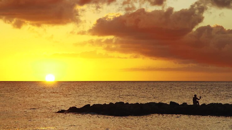 Young woman taking a selfie sitting on the rocks at the beach during a spectacular golden sunset in Curacao, Caribbean