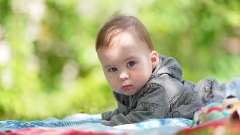 lovely baby boy wearing grey hoody lies on the belly. sweet kid having rest outdoors. blurred backdrop.