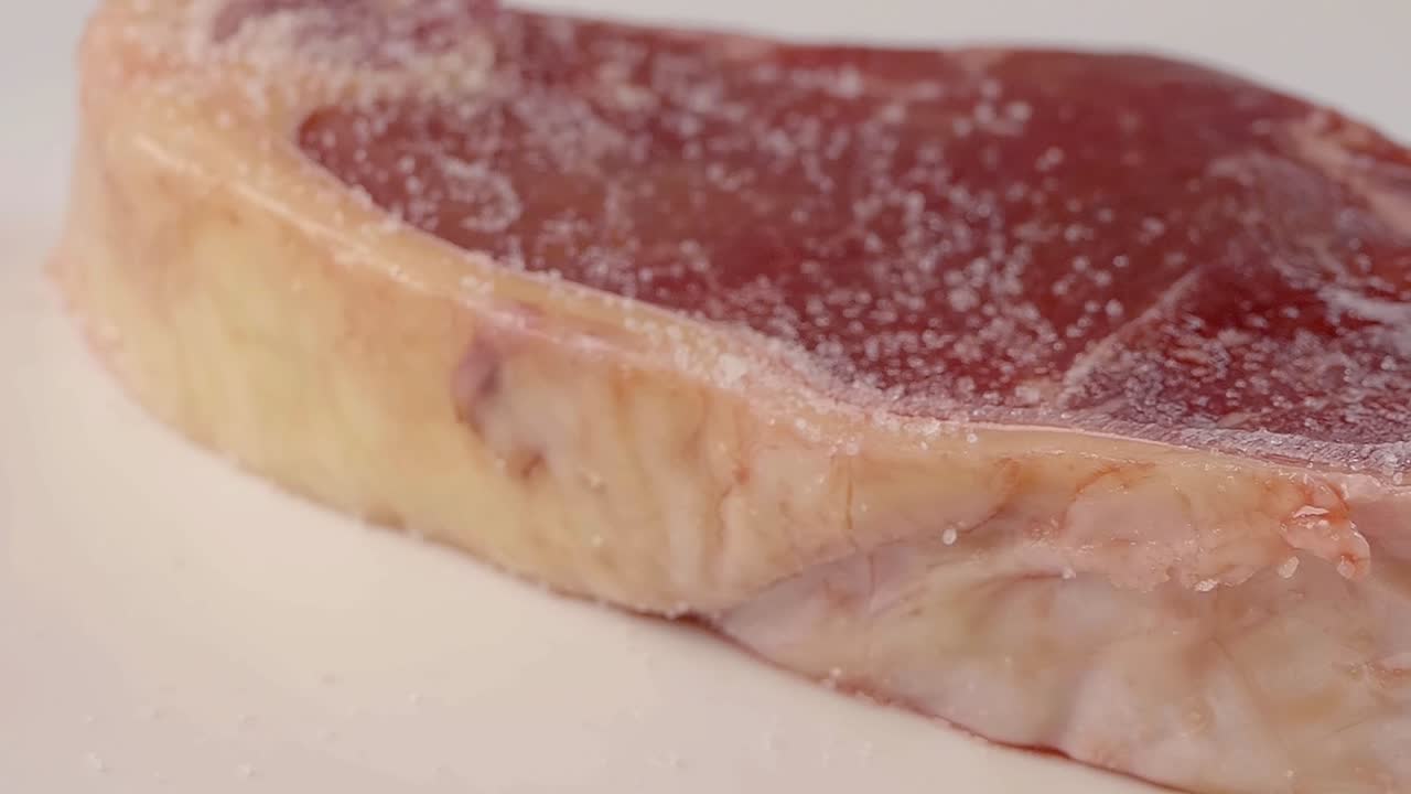 Primo piano al rallentatore della salatura di una bistecca di controfiletto di New York cruda con sale