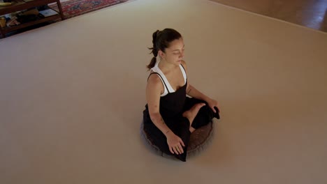 vista lateral angular de una sesión de yoga pacífica con una mujer latina en un estudio geométrico al aire libre, centrándose en el estiramiento y la atención plena sentada con las piernas cruzadas