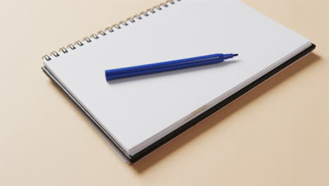 close up of blue marker on notebook with beige background, in slow motion
