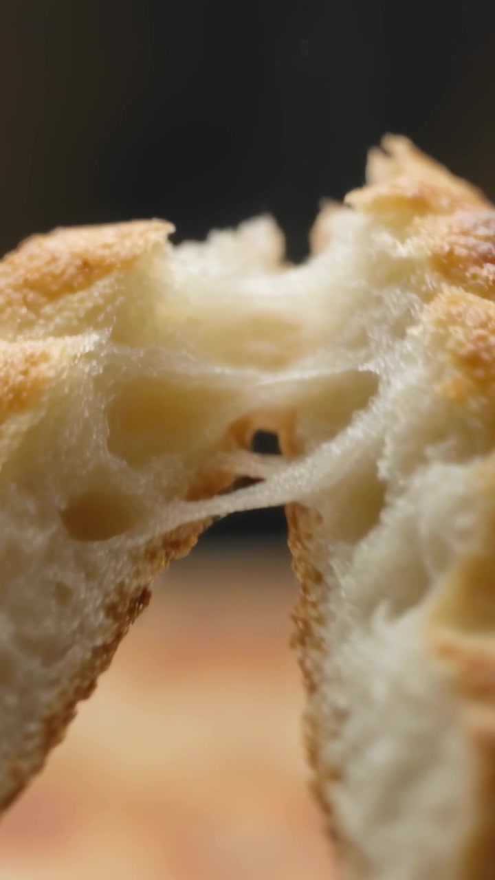 Vertical video: Hidden hand pulling golden bun apart on wood board, revealing elastic crumb