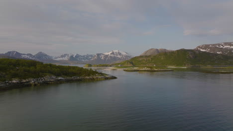 Aerial-push-in-towards-lush-islands,-seagulls-fly-past,-Sommaroya-Bridge-and-mountains-in-background