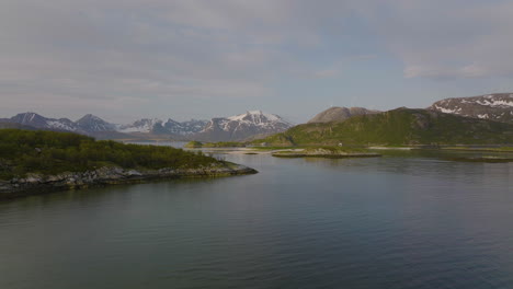 empuje aéreo hacia islas exuberantes, gaviotas volando, el puente sommaroya y las montañas al fondo.