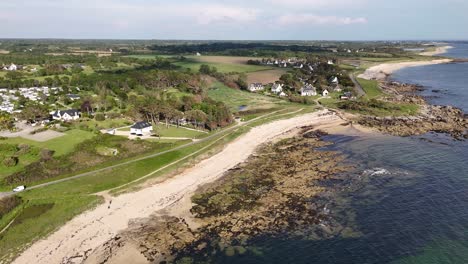 A-coastal-village-with-green-fields,-rocky-shore,-and-clear-blue-water,-aerial-view