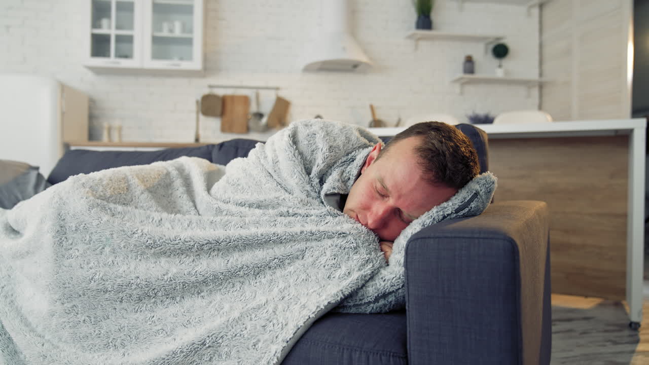 Sick man under warm blanket on comfortable couch at home. Pandemic. Quarantine concept.