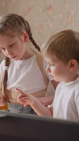 little girl takes brother hand and presses electric piano keys at home lesson. cute children learn music playing with modern digital instrument