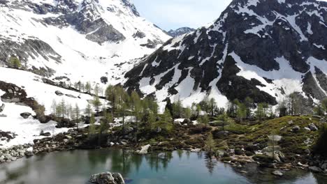 Aerial-view-of-lake-Mässersee-in-the-remote-valley-of-Binntal-in-Valais,-Switzerland-at-the-beginning-of-summer-as-the-surrounding-mountains-are-still-covered-in-snow