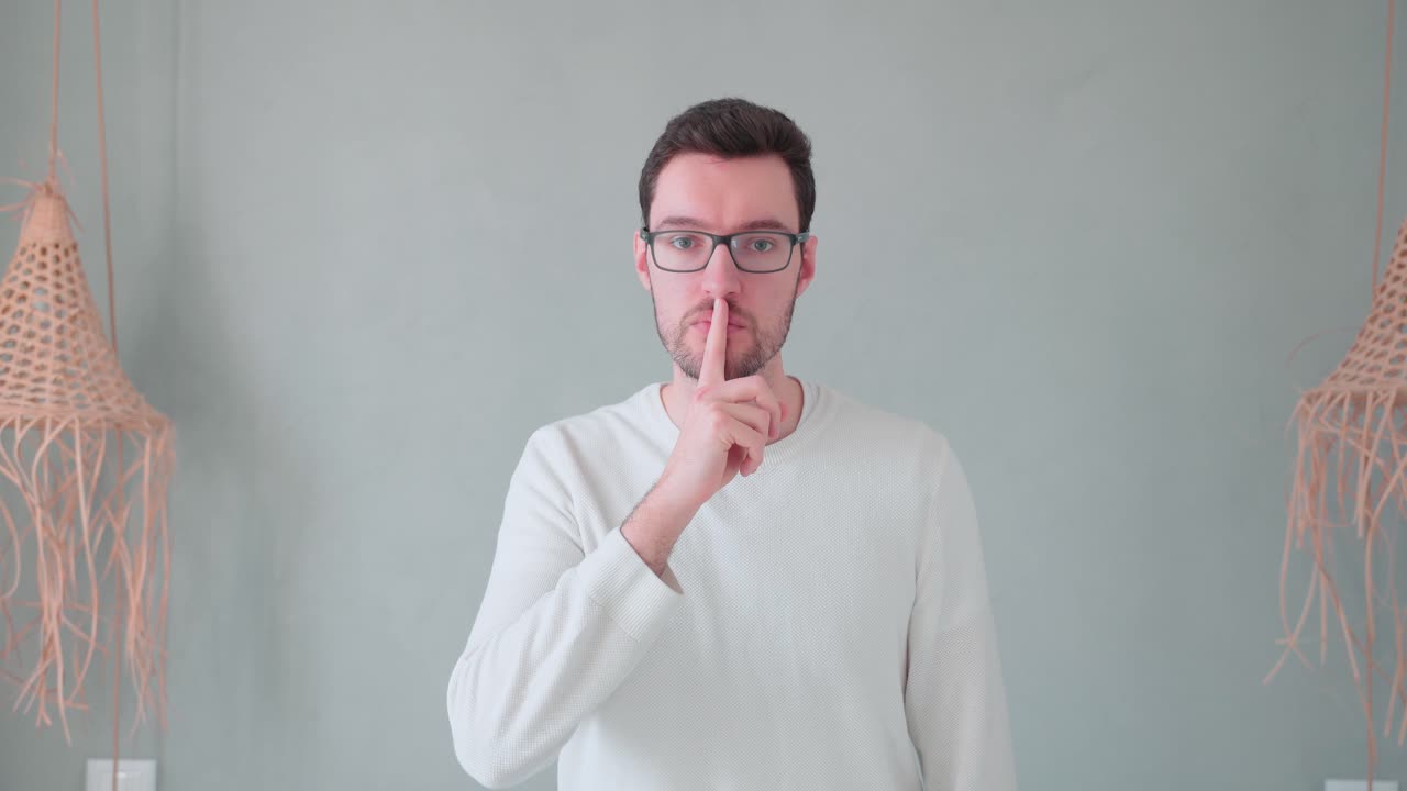 입 앞에서 젊은 남자의 손가락, 차분한 비밀의 표시는 비밀을 유지하고, 말하지 말고, 조용히 하지 마십시오