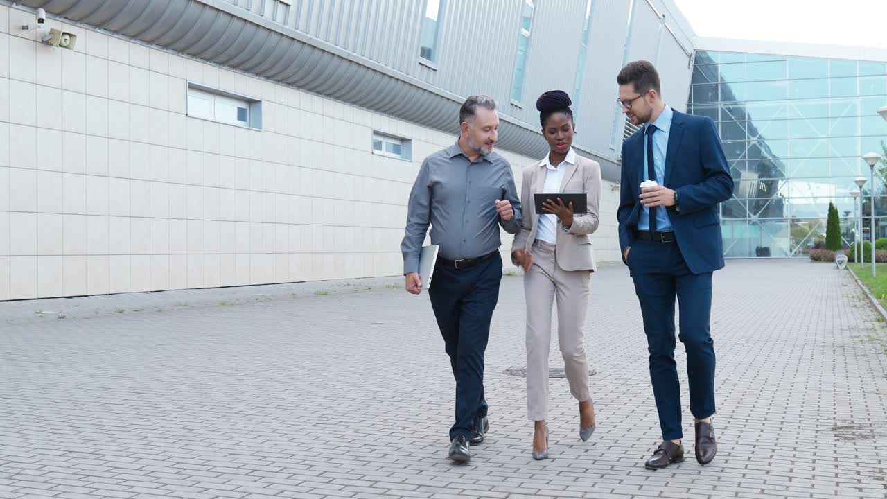 African American young businesswoman and two Caucasian businessmen walking down street and discussing about work using a tablet