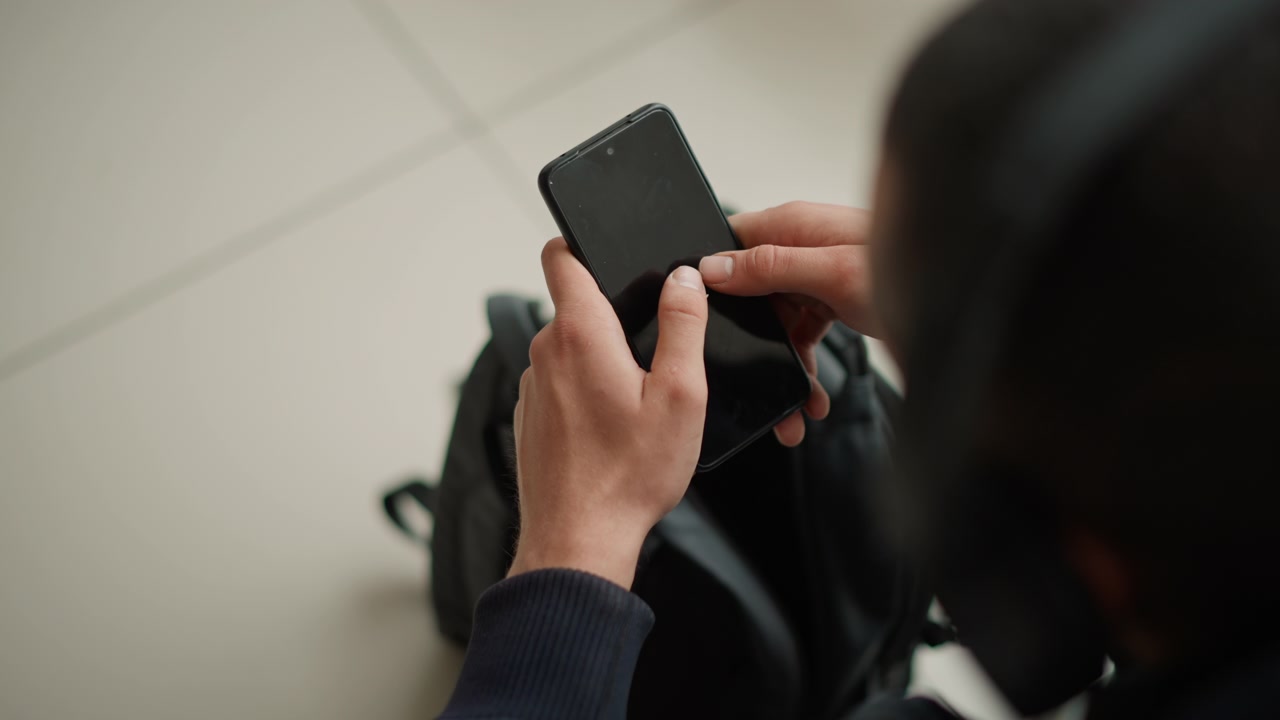 Close up of person holding and interacting with smartphone focusing on hands manipulating device. black backpack is visible in background suggesting travel or daily life context. Soft