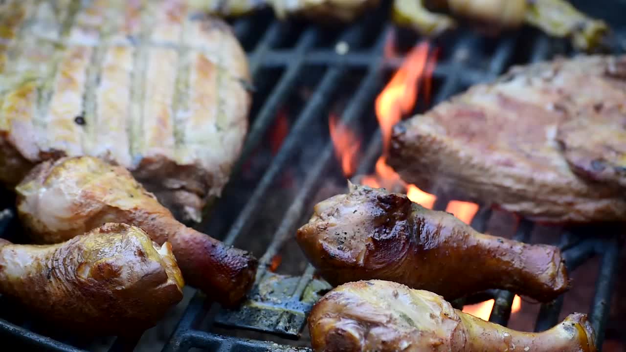 costillas y piernas de pollo frotadas con especias con marcas de parrilla en el primer plano de la parrilla al aire libre que muestra llamas y humo con espacio de copia