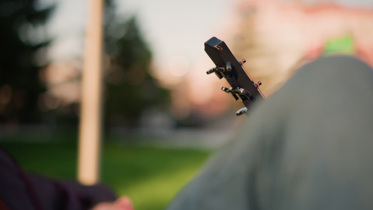 Seren musiker, der hviler fredfyldt udendørs. Fredfyldt guitarist, der slapper af midt i naturen og sollyset. Rolig scene med en musiker, der nyder udendørs ro i de bløde, glødende solnedgangstimer