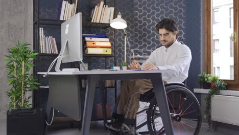 un trabajador discapacitado sentado en una silla de ruedas trabajando en la computadora.