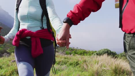 mid section of senior hiker couple with backpacks and hiking poles holding hands and walking