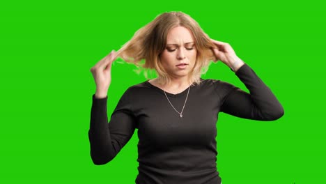 upset blonde woman looks at her damaged hair with splitting ends on green screen