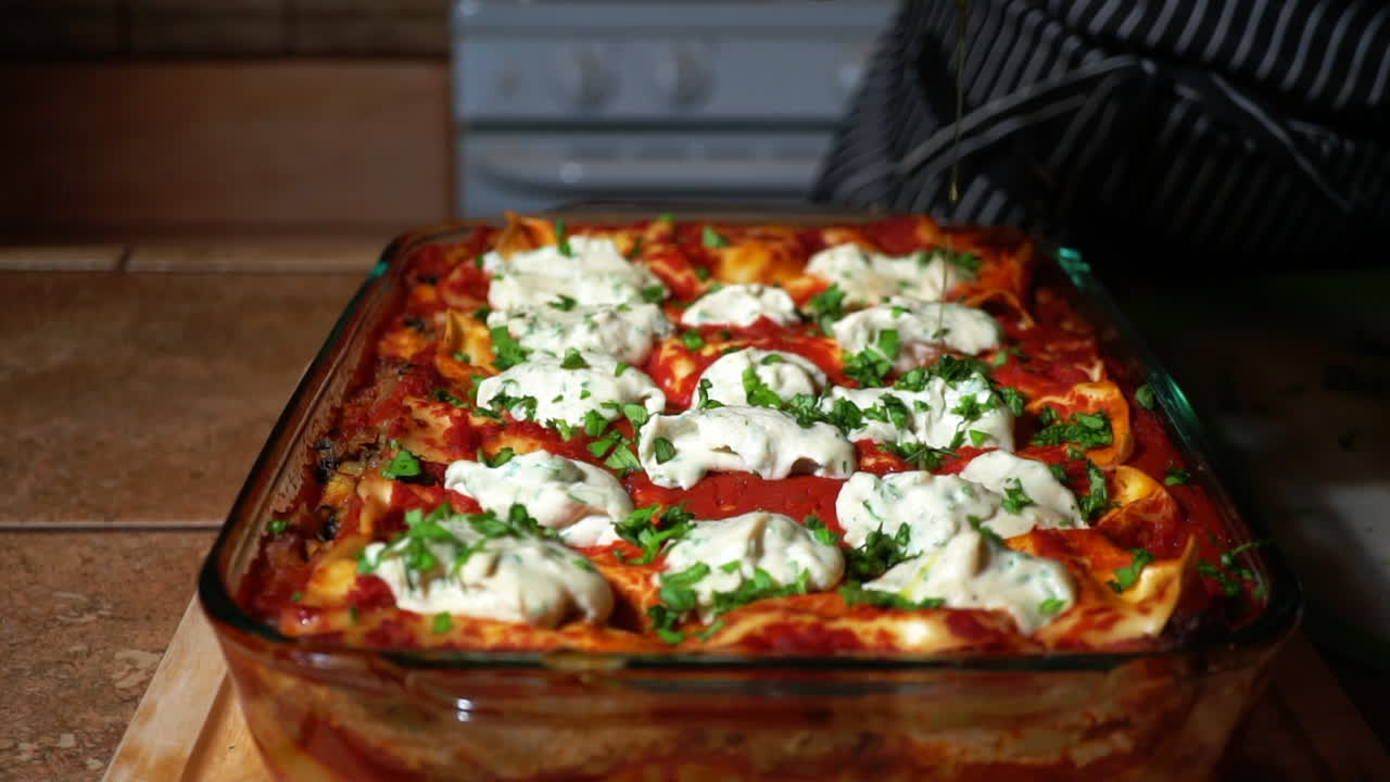 요리사는 유리 팬에 있는 맛있는 구운 라자냐 위에 올리브 오일을 붓습니다.