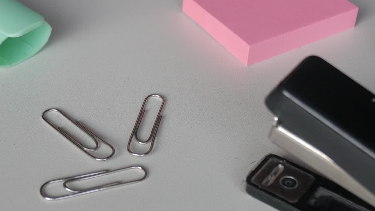 Minimal composition of a mint green marker with metallic paper clips arranged neatly on a white desk in soft daylight