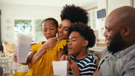 Familia-Comiendo-Palomitas-De-Maíz-En-Casa-Sentados-Juntos-En-El-Sofá-Transmitiendo-Un-Programa-O-Una-Película-A-La-Televisión