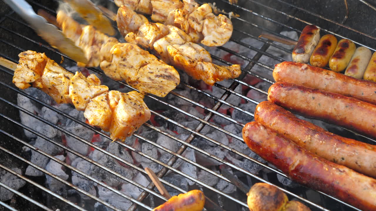 asar salchichas y pollo marinado en la parrilla de barbacoa y girar con pinzas sobre carbón