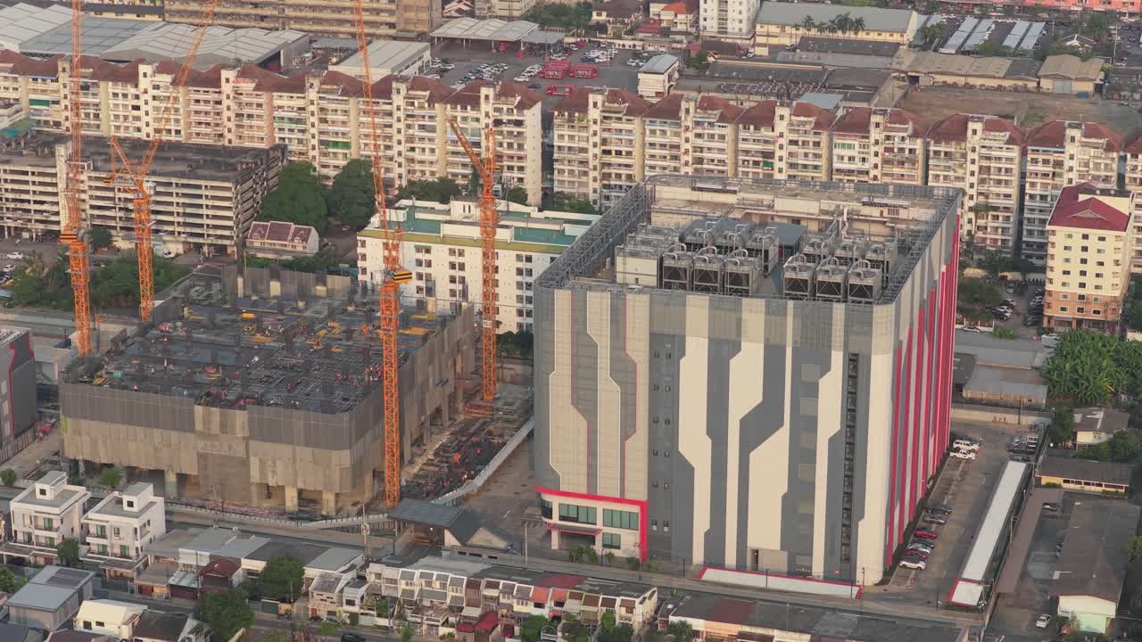 Vista aérea de un gran edificio de centro de datos futurista con sistemas de refrigeración en el techo, junto a una concurrida obra de construcción en Bangkok.