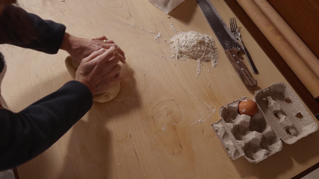 Top-down view of a Romagna cook kneading fresh cappelletti dough by hand on a wooden table. Traditional Italian pasta-making with flour, eggs, and simple kitchen tools