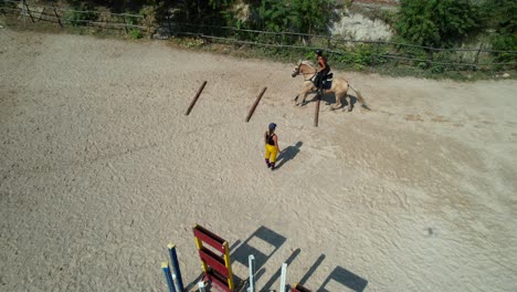 parallax aerial follows a female rider as she clears jumps between three ground bar gaps with trainer watching