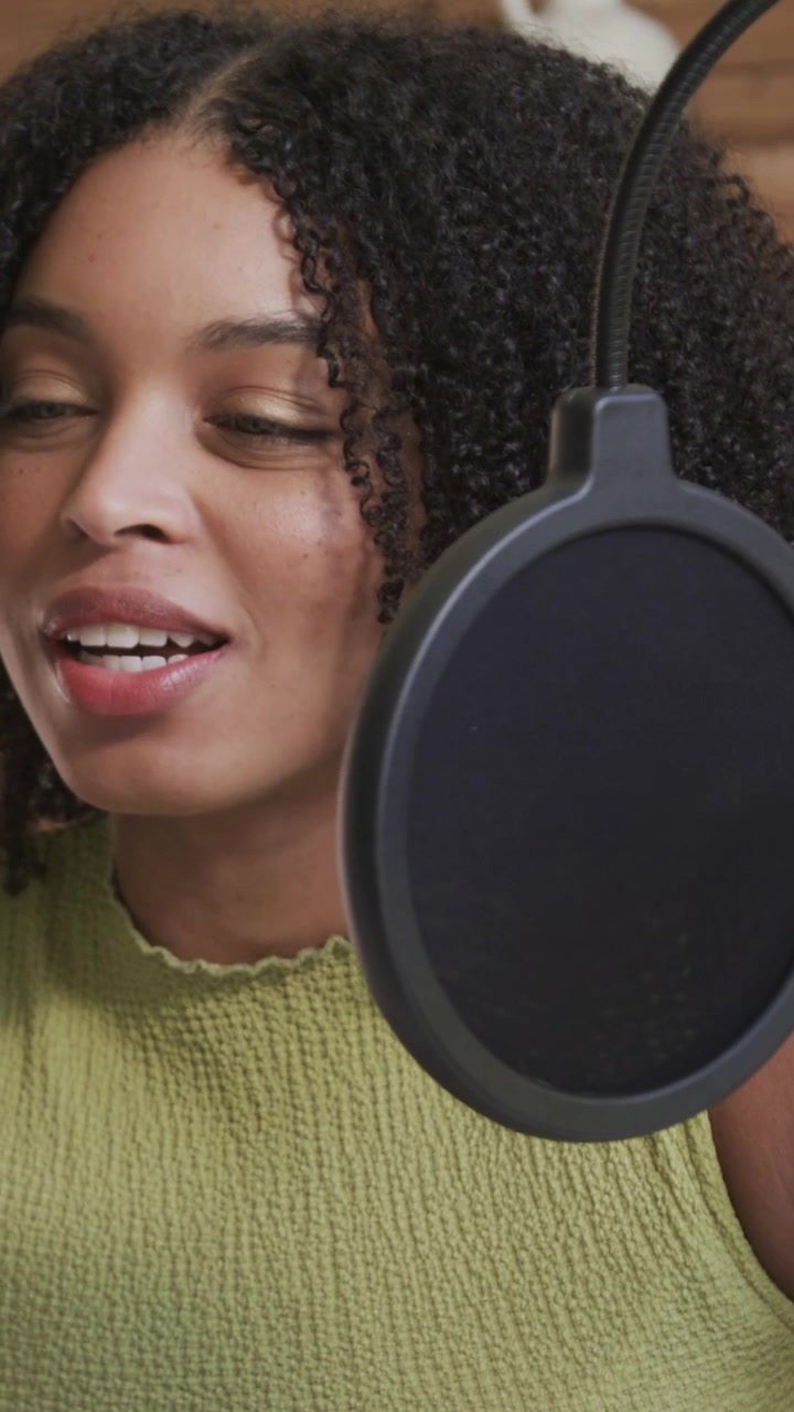 Video verticale: Registrazione, donna con top verde che legge un testo in uno studio casalingo con microfono e filtro anti-pop.