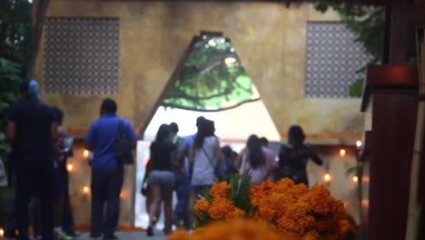 long shot, ornamental flowers are on foreground, people walking on background during celebration of day of the dead