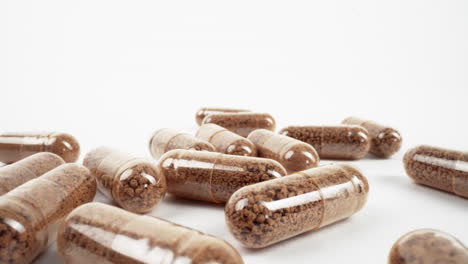 close-up of brown herbal supplement capsules scattered on white background