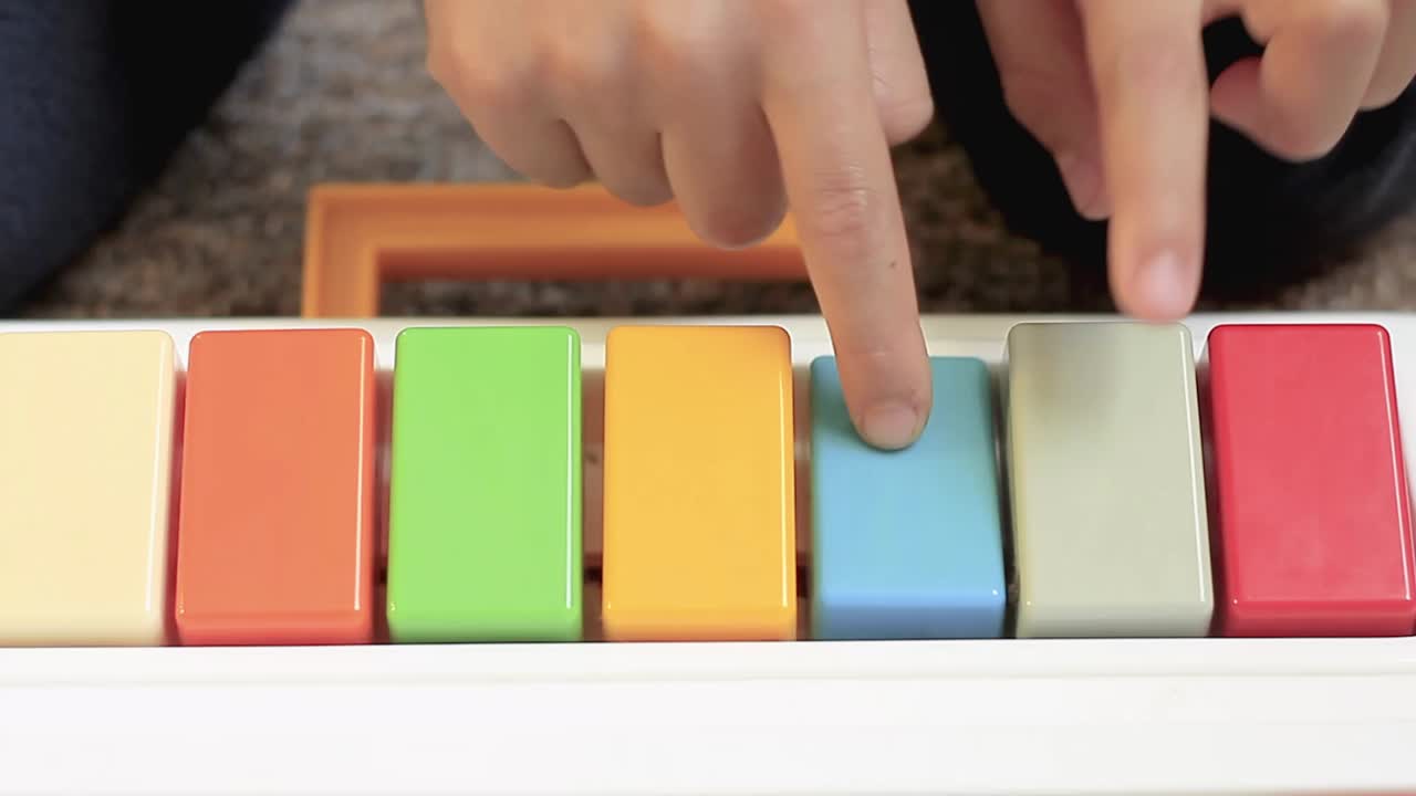 niño tocando el piano de juguete con los colores del arco iris en casa almacen de video