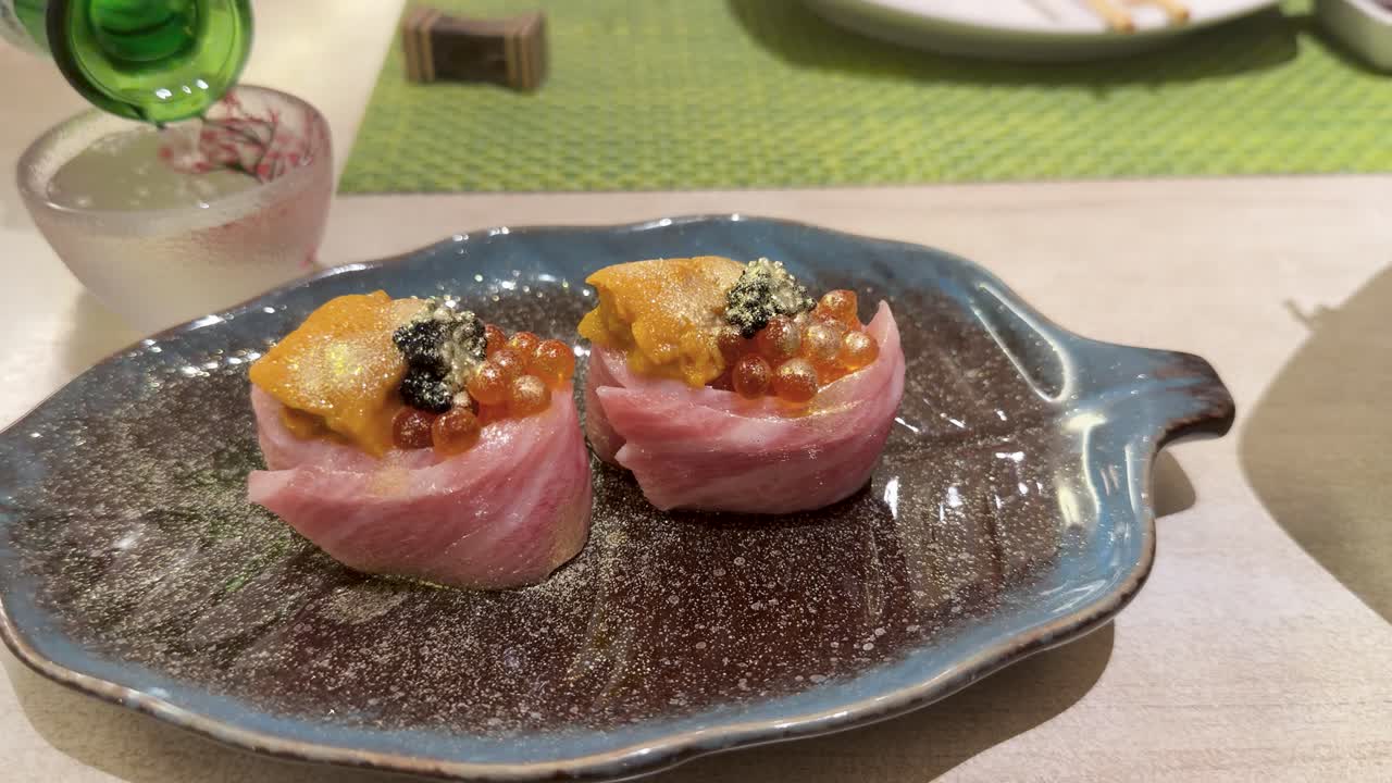 Primo piano di rotoli di sushi premium su un piatto di ceramica mentre il sakè viene versato in un bicchiere