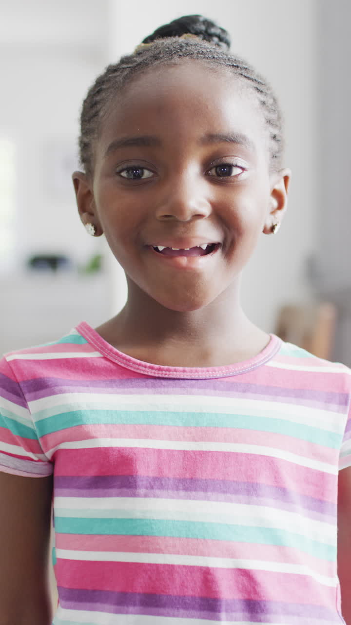 Happy African American girl with braids smiles in vertical video at home, copy space